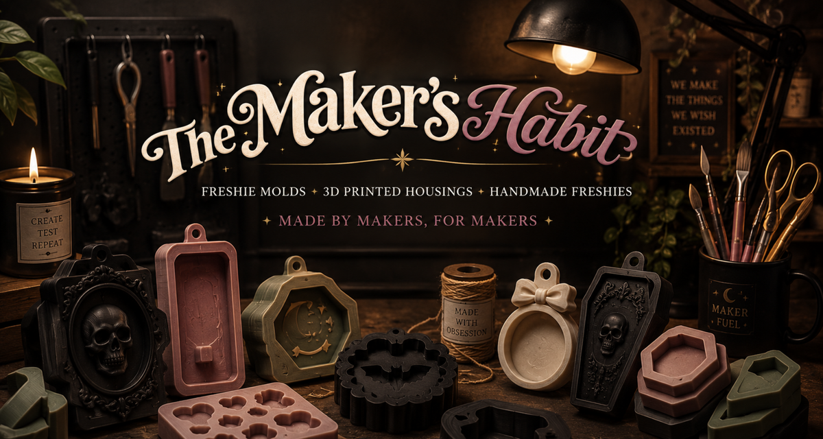 A styled tabletop display of craft supplies and finished handmade items under a warm lamp, with large text reading 'The Maker's Habit' and smaller text 'Freshie Molds, 3D Printed Housings, Handmade Freshies, Made by Makers, For Makers.' Visible products include several pink, black, beige, and green mold-like forms and small crafted objects.